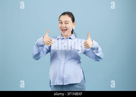 Giovane donna entusiasta che mostra il gesto del pollice alzato con entrambe le mani in studio Foto Stock
