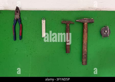Strumenti manuali assortiti tra cui pinze, martello e punte da trapano organizzati su una tavola verde brillante. Foto Stock