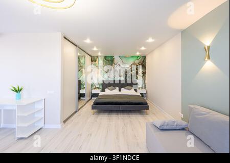 Camera da letto moderna con un letto, carta da parati astratta, armadio con porte scorrevoli, tavolo bianco e decor minimalista Foto Stock