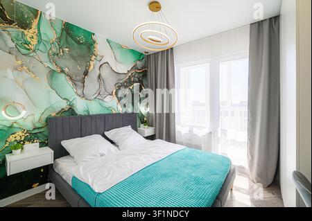 Camera da letto accogliente con un letto, illuminazione moderna e carta da parati verde/oro appariscente. Luce naturale Foto Stock