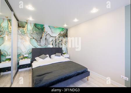 Camera da letto moderna con letto grigio scuro, parete accentata astratta verde e oro, armadio con porta scorrevole con specchio e comodini sospesi bianchi Foto Stock