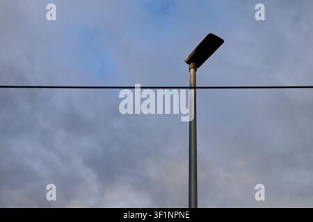 Lampione minimalista contro un cielo nuvoloso drammatico con cavo sospeso e infrastrutture urbane Foto Stock