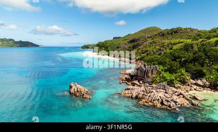 Massi di granito lungo una costa verdeggiante e lussureggiante, che portano a una spiaggia sabbiosa isolata. Curieuse, Seychelles. Foto Stock