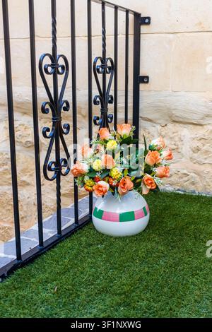 Mazzo di rose arancioni in vaso di ceramica accanto a una ringhiera in ferro battuto su un piccolo balcone Foto Stock