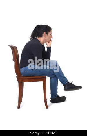 Vista laterale di una donna seduta su una sedia, con la mano sul mento e le gambe incrociate su uno sfondo bianco Foto Stock