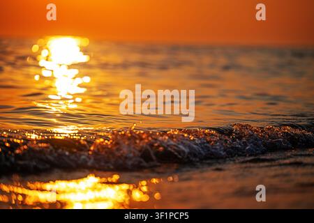 Tramonto dorato sulle onde dell'oceano con riflessi d'acqua scintillanti, sfondo di paesaggio marino caldo con spazio per il testo Foto Stock