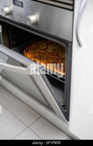 Un forno con la porta aperta che mostra una pizza fatta in casa appena cotta Foto Stock