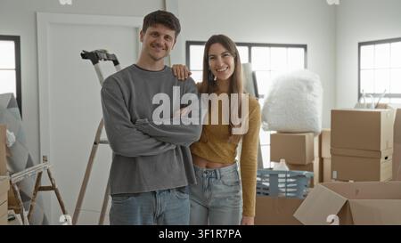 Uomo e donna si trovano tra scatoloni di cartone, scala e cesto per bucato, donna sorridente a mano sulla spalla dell'uomo mentre disimballano nell'edificio e si muovono Foto Stock