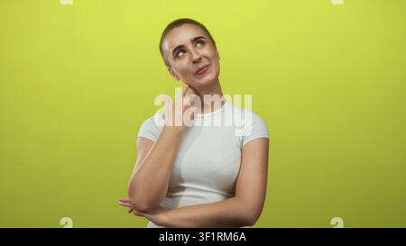 Donna che tocca il collo con il dito e sorride mentre guarda in alto in uno sfondo verde studio; curiosità premurosa. Foto Stock
