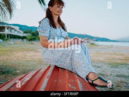 DONNA ANZIANA CON UN LIBRO SULLA SPIAGGIA Foto Stock
