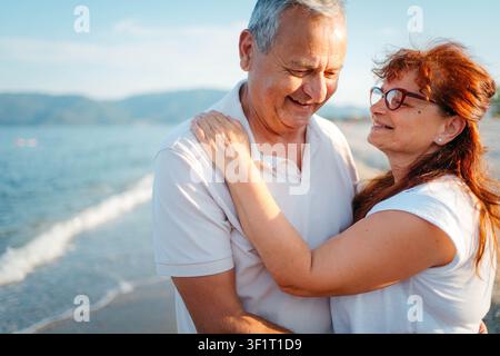 Coppia di anziani seduti abbracciati sulla spiaggia Foto Stock