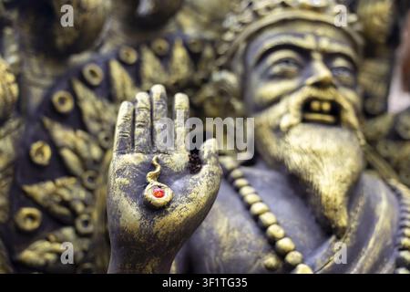 Una mano di statua dorata sollevata in segno di benedizione con una gemma rossa e perle ornate, primo piano di una scultura metallica erosa che trasmette riverenza e spirito antico Foto Stock