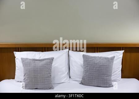 Due cuscini decorativi grigi su un letto bianco con testiera in legno, scena di camera da letto minimalista e accogliente che trasmette calma e comfort Foto Stock