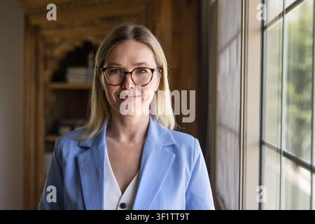 Donna caucasica che sorride alla telecamera posando in un ufficio domestico Foto Stock
