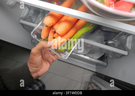 Mano che raggiunge carote e peperoni in un frigorifero Foto Stock