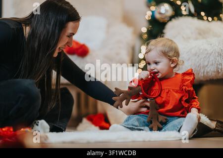 Madre e bambina condividono un momento gioioso giocando con un renna di peluche accanto all'albero di Natale Foto Stock