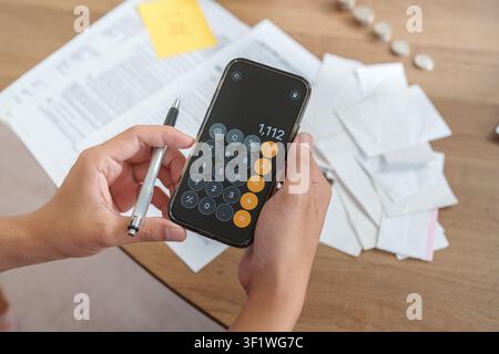 Mani ritagliate che utilizzano un'app calcolatrice su uno smartphone per la pianificazione fiscale Foto Stock