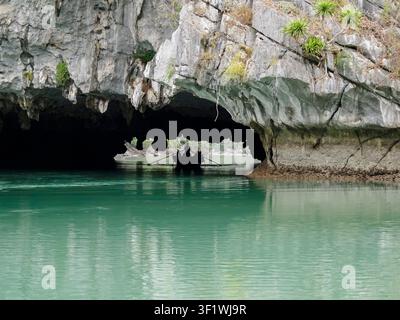 Piccola barca a remi in silhouette all'interno di una grotta di calcare sull'acqua smeraldina calma della baia di Lan Ha, Vietnam. Foto Stock
