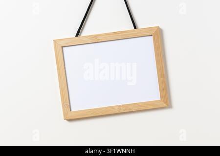 Lavagna bianca vuota con cornice di legno appesa a un muro bianco. Modello di template Foto Stock