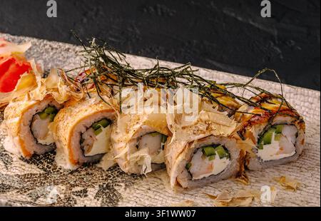 Rotoli di sushi giapponesi con salmone, gamberetti, formaggio fresco e cetriolo, guarniti con bonito e nori Foto Stock