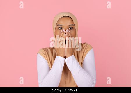 Giovane donna musulmana nera sorpresa con hijab che copre la bocca con entrambe le mani Foto Stock