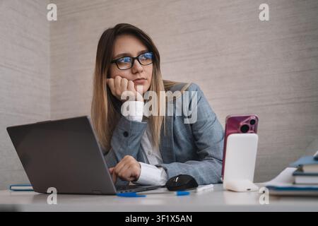 Donna d'affari pensierosa che appoggia il mento sulla mano, distogliendo lo sguardo da un laptop in un ufficio moderno. Contemplazione, sogno ad occhi aperti in ufficio e un momento Foto Stock