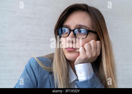Donna d'affari stanca che guarda pensierosa nel vuoto, appoggiando il mento sulla mano. Burn-out, stress, mal di testa e profonda contemplazione aziendale. Pensatrice Foto Stock