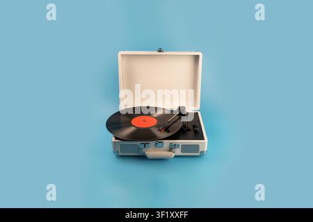 Un giradischi classico in stile valigia è aperto, mostrando un vinile rotante e il braccio di lettura su uno sfondo blu solido Foto Stock