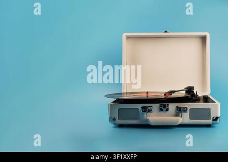 Un giradischi in stile retrò è aperto, con un disco in vinile nero che suona sul suo piatto, su uno sfondo blu solido Foto Stock