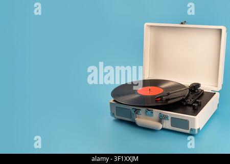 Un giradischi portatile classico con un vinile nero e etichetta rossa è aperto su uno sfondo blu brillante, pronto per suonare Foto Stock