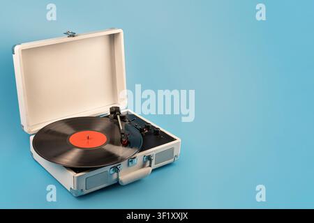 Un giradischi classico con un disco in vinile nero ed etichetta rossa è aperto su uno sfondo blu brillante, evocando la nostalgia per l'audio analogico Foto Stock