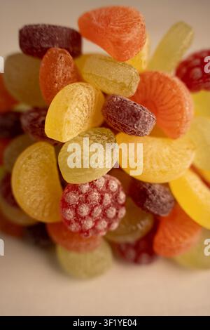 Macro close-up di colorati caramelle dure e gommose assortite al gusto di frutta ammucchiate in una ciotola da tavolo, illuminazione calda e soffusa che mette in risalto le texture zuccherine Foto Stock