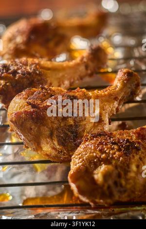 cosce di pollo al BBQ cotte al forno su una griglia metallica, pelle dorata croccante e succhi che gocciolano in primo piano e con effetto sfocato Foto Stock