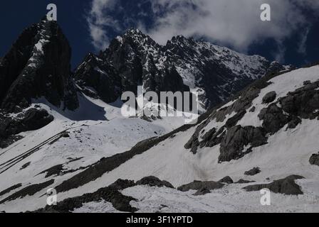 Una catena montuosa innevata con picchi affilati sotto un cielo parzialmente nuvoloso. Foto Stock