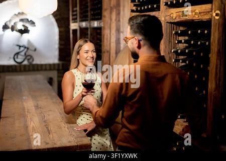 Due amici si godono una deliziosa esperienza di degustazione del vino in una cantina affascinante piena di bottiglie. L'atmosfera calda crea un ambiente perfetto. Foto Stock