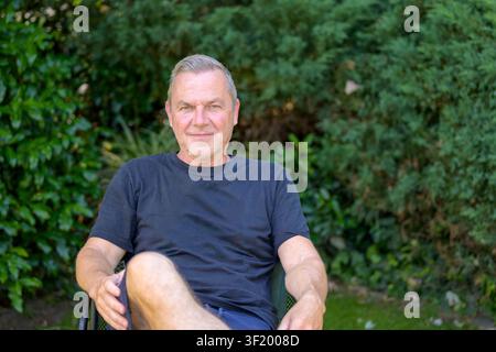 Uomo di mezza età che si rilassa in giardino godendosi una giornata estiva pacifica e soleggiata. Foto Stock