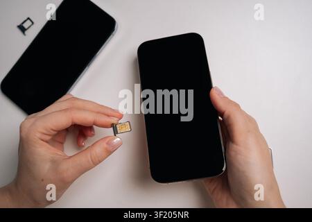 Donna che tiene una scheda SIM e un nuovo smartphone su un tavolo bianco, preparandosi a inserire la scheda SIM e ad attivare il servizio mobile per una connettività senza interruzioni e Foto Stock