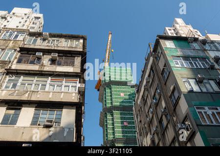 Cantiere edile con un grattacielo ricoperto da una rete verde, situato tra edifici residenziali più antichi. Kowloon, Hong Kong Foto Stock