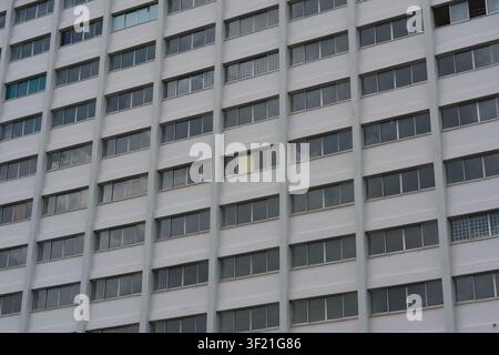 Edificio alto con finestre uniformi e una finestra gialla. La facciata grigia presenta un motivo architettonico ripetitivo. Le finestre sono disposte in file ordinate Foto Stock