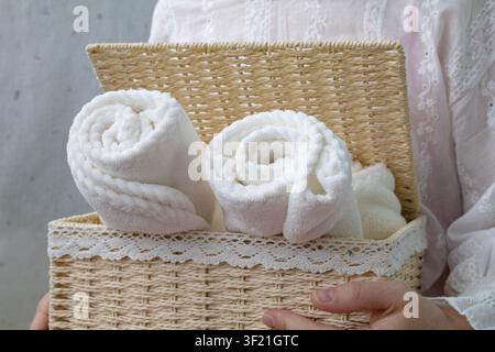 Donna che tiene un cesto di vimini pieno di asciugamani freschi piegati Foto Stock