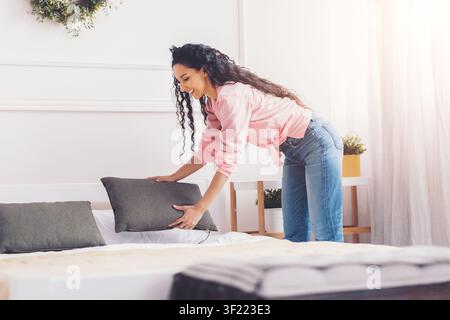 Giovane donna che organizza cuscini sul letto in una camera da letto accogliente, concetto di arredamento domestico Foto Stock