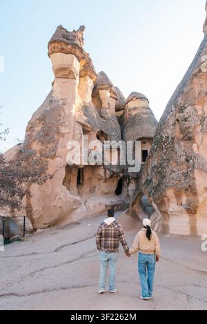 Una coppia cammina mano nella mano, esplorando peculiari camini fatati e antiche abitazioni rupestri nella Cappadocia, Turchia. Lo splendido paesaggio offre uno sfondo incantevole per la loro avventura vacanza. Foto Stock
