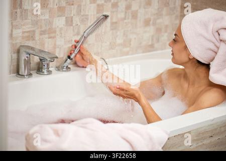 Donna che si gode un bagno schiumoso applicando acqua sul braccio Foto Stock