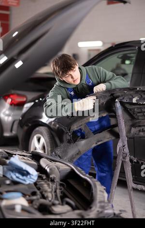 Giovane meccanico specializzato che ripara il paraurti rimosso in officina Foto Stock