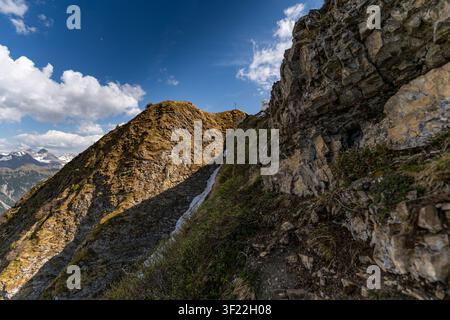 Una vista grandangolare cattura i ripidi pendii rocciosi e le creste erbose del monte Fellhorn nelle Alpi di Allgäu sotto un cielo blu intenso. Una scogliera drammatica Foto Stock