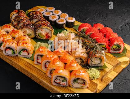Diversi tipi di sushi sono disposti su una tavola di legno. Il sushi include rollini con varie farciture e condimenti. Il wasabi verde è servito come contorno. Foto Stock