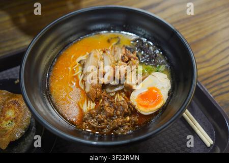 Delizioso ramen al pollo piccante con uovo sodo, noodles e condimenti servito in una ciotola nera su un vassoio Foto Stock