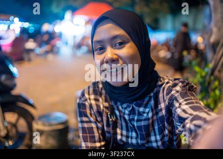 Ritratto di una giovane donna musulmana sorridente in hijab che scatta un selfie all'aperto di notte con luci della città in bokeh. Foto Stock