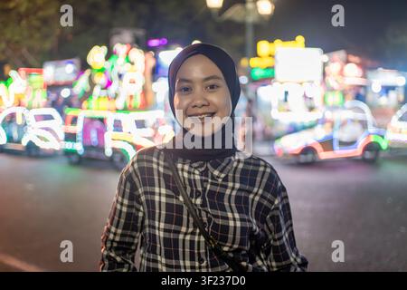 Ritratto di una giovane donna musulmana sorridente con hijab e luci colorate della città illuminate sullo sfondo. Foto Stock