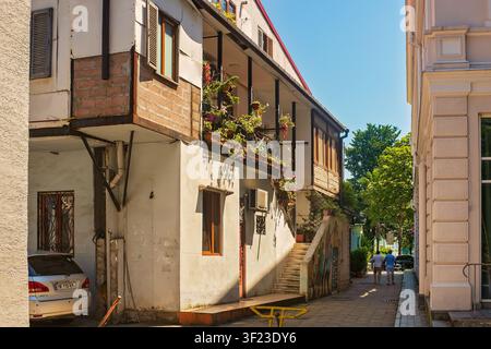 Batumi, Georgia - 1 luglio 2026: Edificio residenziale tradizionale con balcone in legno decorato con piante verdi in una stretta e accogliente strada del centro storico. Foto Stock